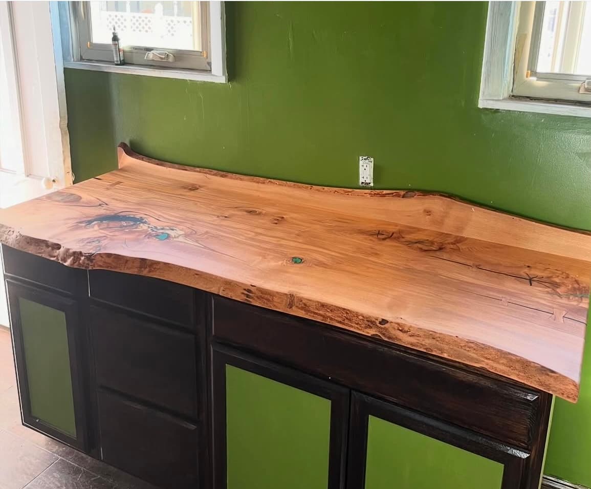 Live edge epoxy surface built by Tougas Timberworks against green cabinets
