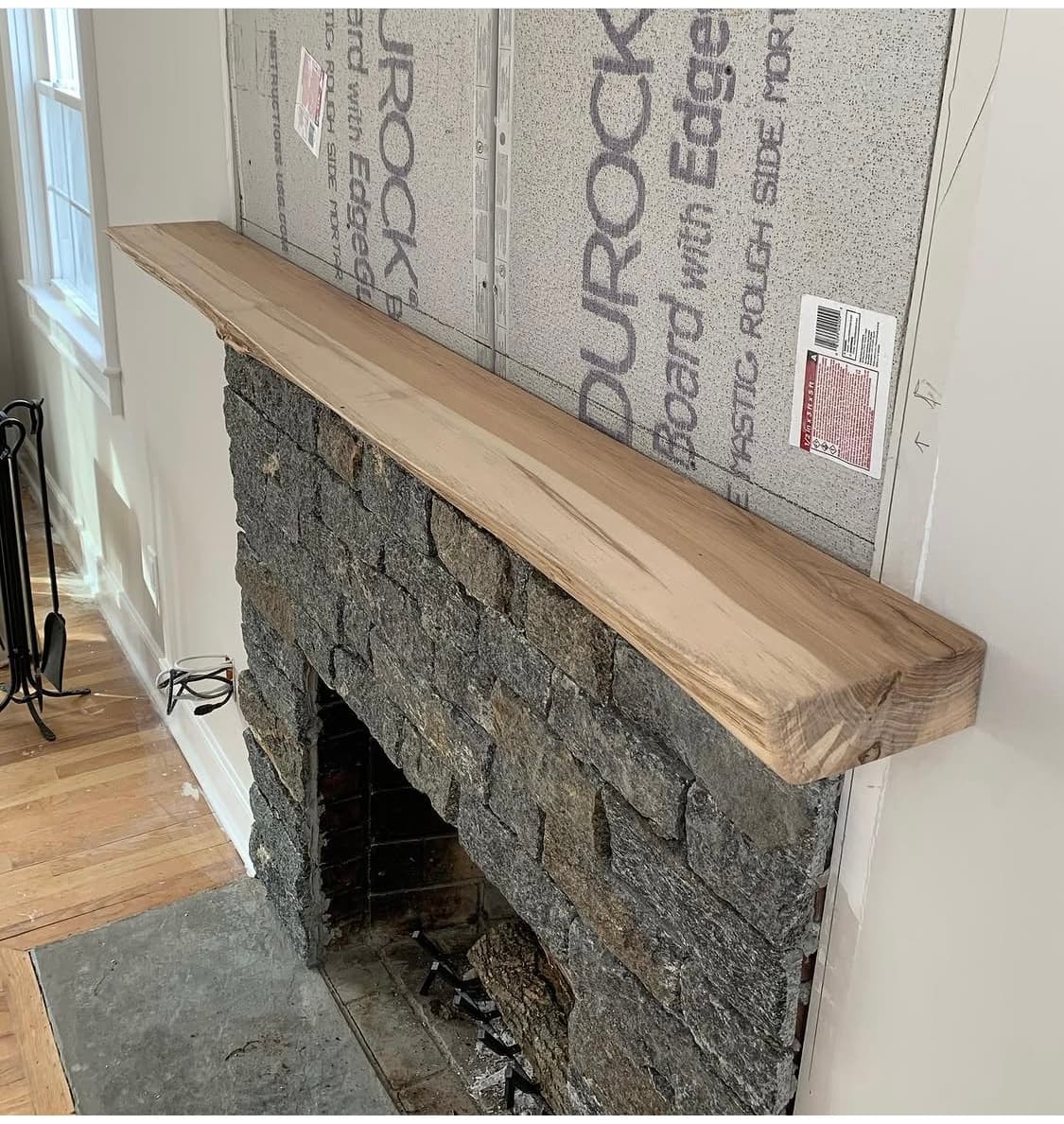 Live edge mantel mounted on a stone fireplace during construction